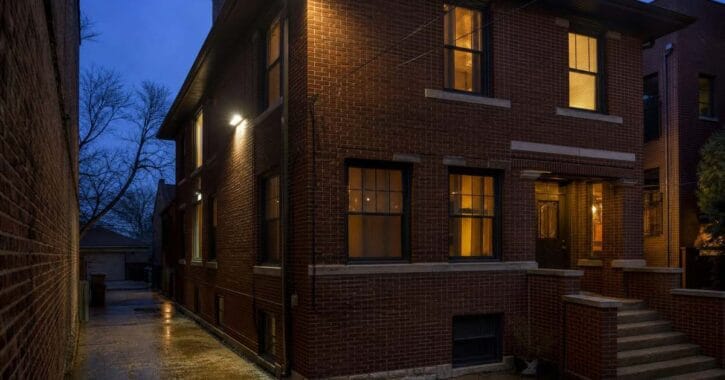 Security Lighting Installation 1 LED wall-pack and flood security lighting on a brick two-flat at dusk