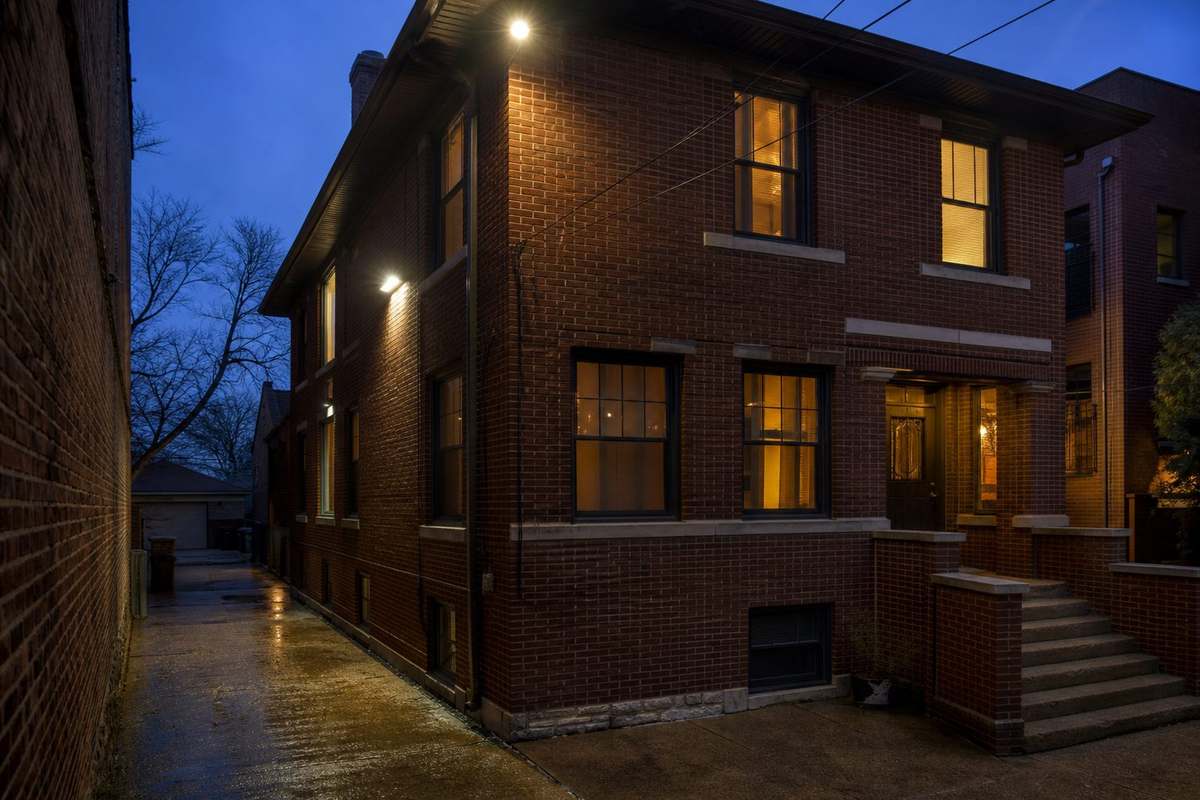 Security Lighting Installation 2 LED wall-pack and flood security lighting on a brick two-flat at dusk